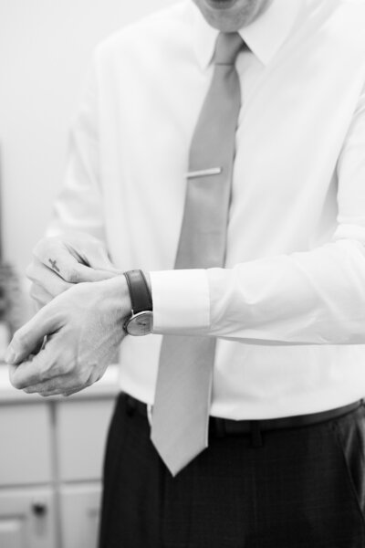 A black and white detail of the groom getting ready, fastening his watch before his wedding ceremony in North Carolina, by destination wedding photographer My Sun and Stars Co.