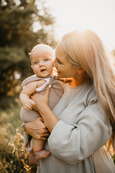 Mother holding baby outside in a field looking happy