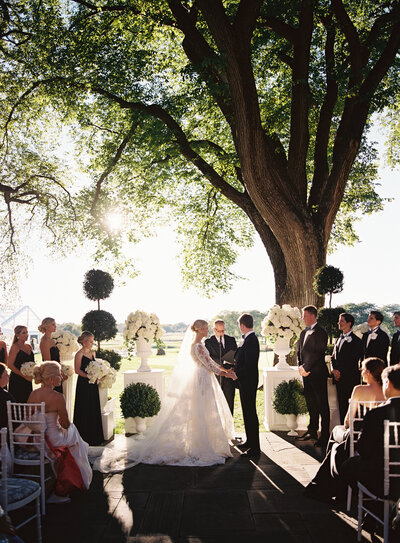 Bride holding a bouquet of fresh white lilies and greenery, tied with a white ribbon.
