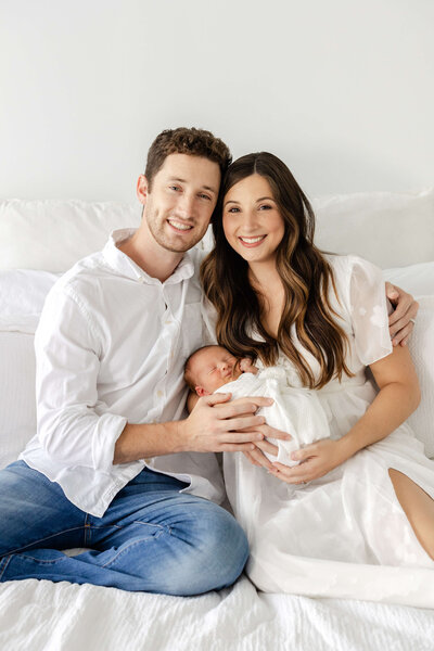 Mother and father smiling at the camera while holding their newborn during newborn photography session