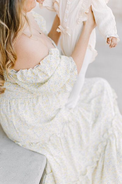 A detail photo of a light yellow floral dress that a young mother is wearing while lifting up her baby daughter