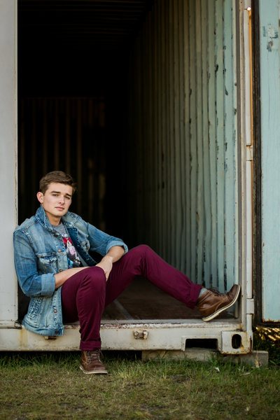 High school boy sits in the back of a trailer during senior portraits