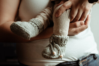 Ausschnitt einer Newborn Homestory. bei der die frisch gebackene Mama ihr Baby im Arm hält.