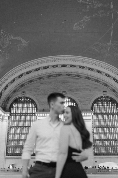 Elegant black and white film-style engagement photo of a couple at Grand Central Station in New York City.