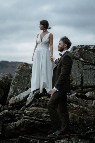 Couple stand on a rock and hold hands after their wedding in Loch Lomond, Scotland