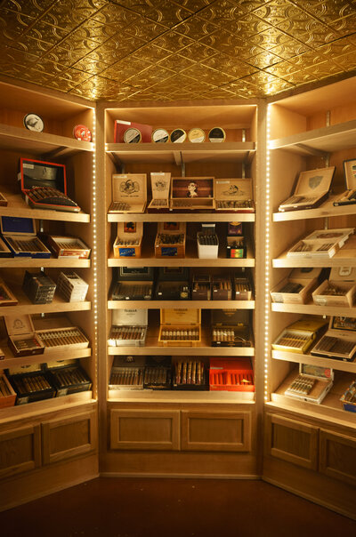 Cigar lounge humidor featuring custom built cabinetry, LED lighting, decorative metal ceiling and a selection of cigars.