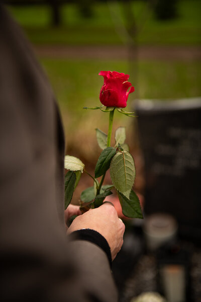 Vrouw voor een graf met een rode roos in haar hand.