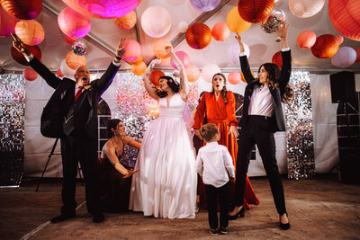 A bride parties with her guests in a vibrant reception tent filled with colorful lantern ball decor