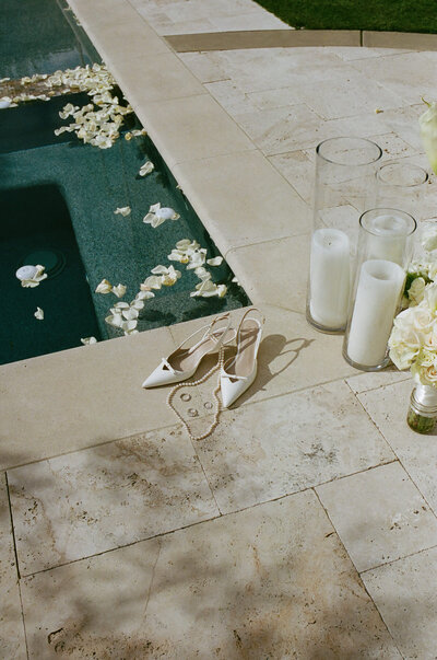 photo of bride's shoes sitting next to a pool along with white candles in glass pillars taken by Wine country wedding photographer