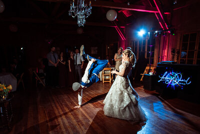 Bride watches her husband do hip-hop dance on the dance floor at wedding reception.