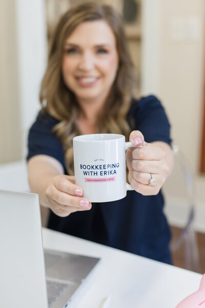 Erika holding out a cup of coffee in a mug with her logo on it