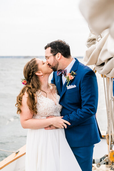 Couple kissing on a sailboat during their wedding. Photo by their Maine wedding photographer.