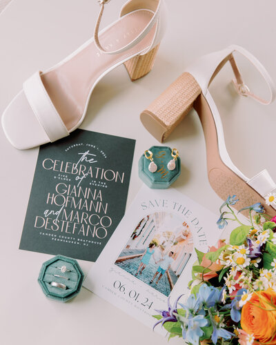 Wedding invitations, heels, rings, jewelry, and flowers laid out together 
