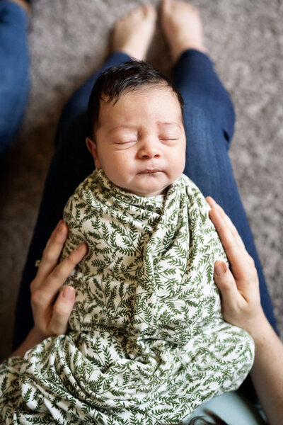 Swaddled baby on mother's lap while she is touching his arms