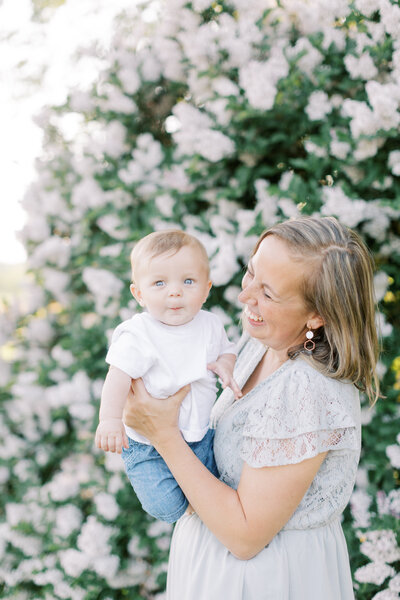 Mother holding baby in front of a lilac bush