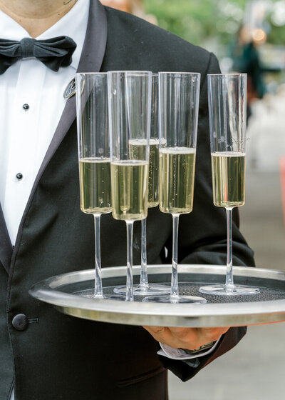 Server in a tuxedo holding a tray of champagne glasses.