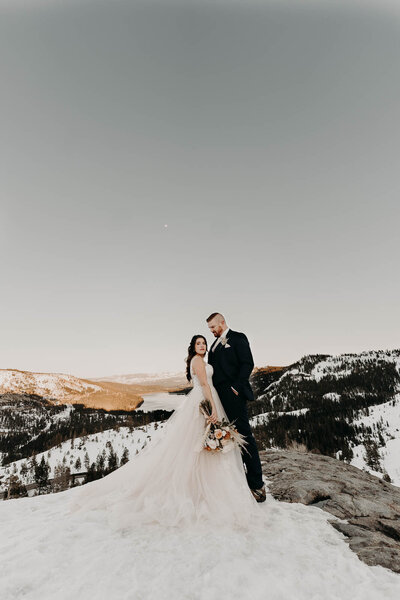 a bride & groom posing in front of a mountain view with the bride's train lays in the foreground