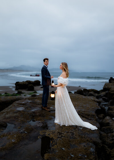 Couple holding lanterns on a rocky Pacific Northwest coast during a styled shoot for adventurous photographers.