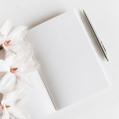 blank white notebook with silver pen beside it and large white floral blooms