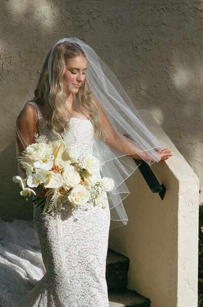 Bride holding a white floral bouquet in golden sunlight, reflecting a peaceful moment during a luxury wedding weekend experience.