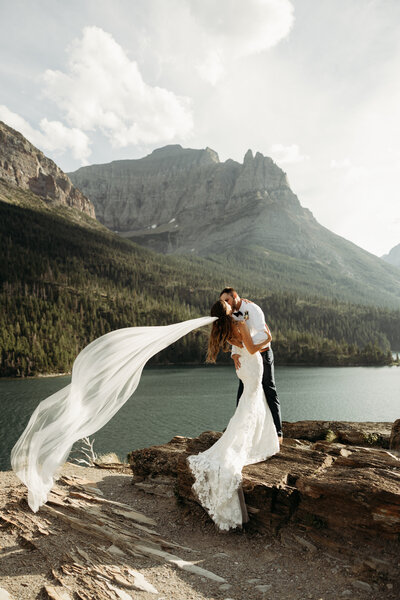 couple eloping in glacier national park on a rock surrounded by water