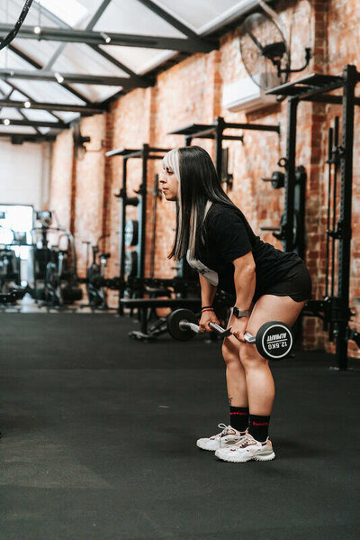 Deadlift Exercise in Melbourne Gym: A woman performing a barbell deadlift in a spacious Melbourne gym with a brick-wall interior and industrial-style design.