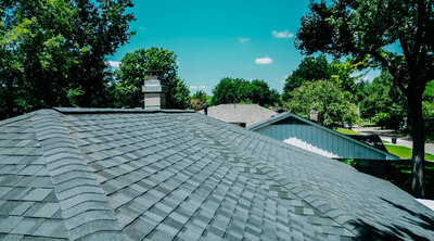 A beautiful new roof built by United Contractors of Texas sits before a clear blue sky and lush green trees
