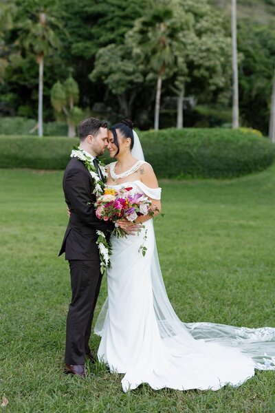A wedding couple standing forehead to forehead in a green field 