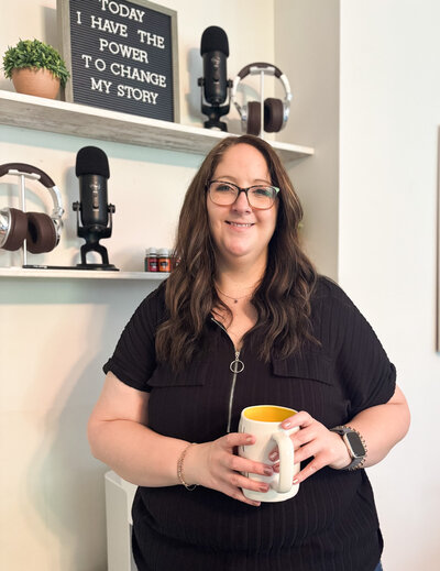 Marketing strategist smiling with coffee mug in hand in front of podcast setup.