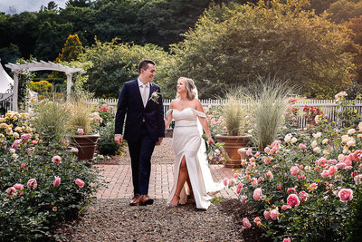 Bride and groom walking through beautiful rose garden atthe gardens at the uncanoonuc mountain by Lisa Smith Smith