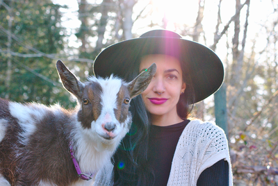 Animal Communicator wearing large brimmed hat and her spotted goat standing beside each other. 