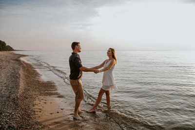 Engaged couple dancing in the shoreline at Grand Bend beach for engagement photoshoot. They are looking at each other and the image is of their side profile.