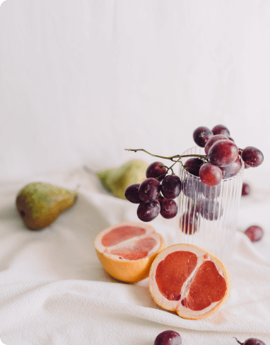 An assortment of fruits including grapefruit, purple grapes, and pears on a white cloth.