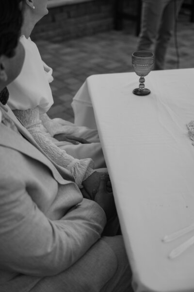 Bride and groom holding hands during the speeches at their wedding in black and white.