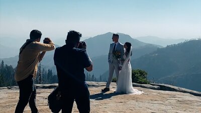 A white bride and groom standing in Sequoia Park while a videographer films their wedding.