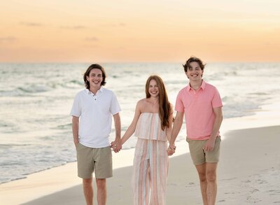 Professional photo on beach of 3 older siblings holding hands and smiling. Photographed at Santa Rosa Beach, FL.