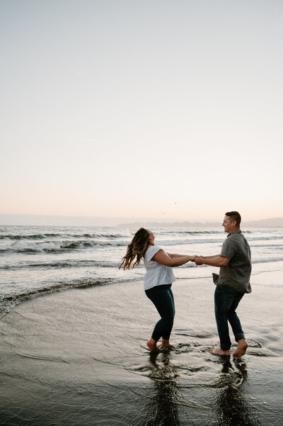 Beachside engagement session with couple laughing and splashing in the waves