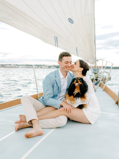 Bride, groom, and their American Cocker Spaniel sitting on the deck of a sailboat and smiling while the boat is sailing on the Atlantic Ocean