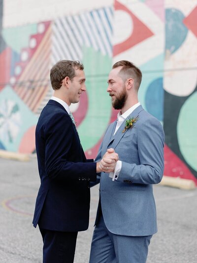 The grooms embracing against brightly painted wall during their same sex marriage in Baltimore