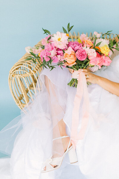 Bride crossing her legs in a chair holding a bright pink flower bouquet