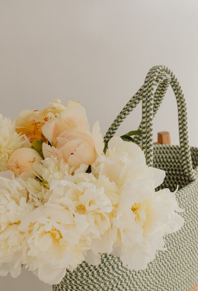 A woven basket filled with soft white and cream peonies, creating a delicate floral arrangement.