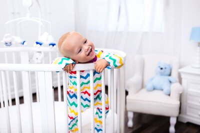 baby leaning standing up leaning on crib  walls smiling