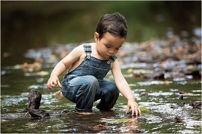 little boy in overalls playing in the creek