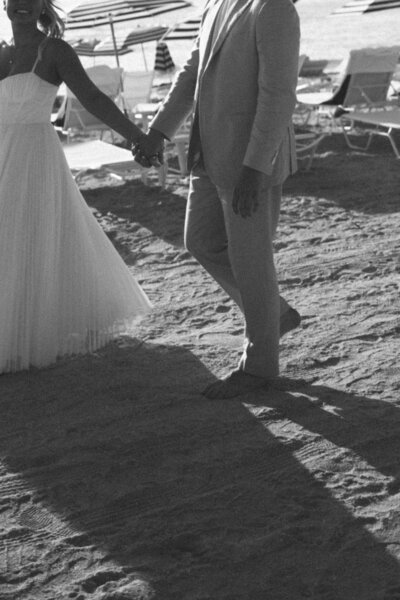 Bride and groom holding hands on the sandy shores of The Beach Club Longboat Key, Florida—an intimate and elegant waterfront wedding moment, planned by Watters & Co. Events.