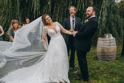 a bride and groom laugh during their ceremony as her veil flies all over the place