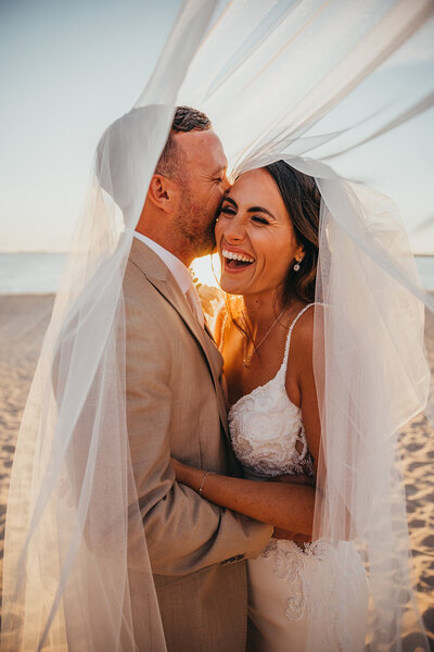 bride and groom laugh under veil
