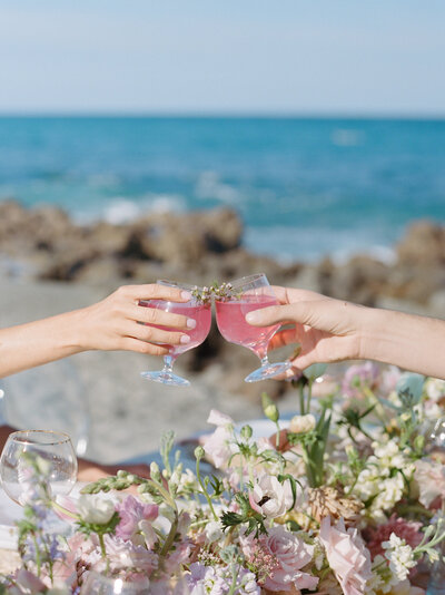 Two glasses of pink cocktails clinking at a beach