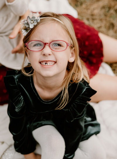 Young girl wearing glasses, a boy, and dark green dress looking at the camera smiling outside in Annapolis Maryland.