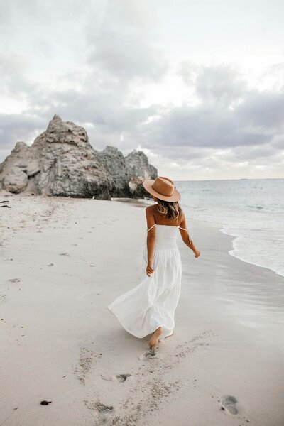 Woman in a white summer dress and hat walking on the shore line