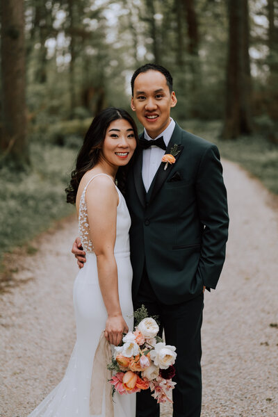 Bride and groom standing on a path smiling at the camera.
